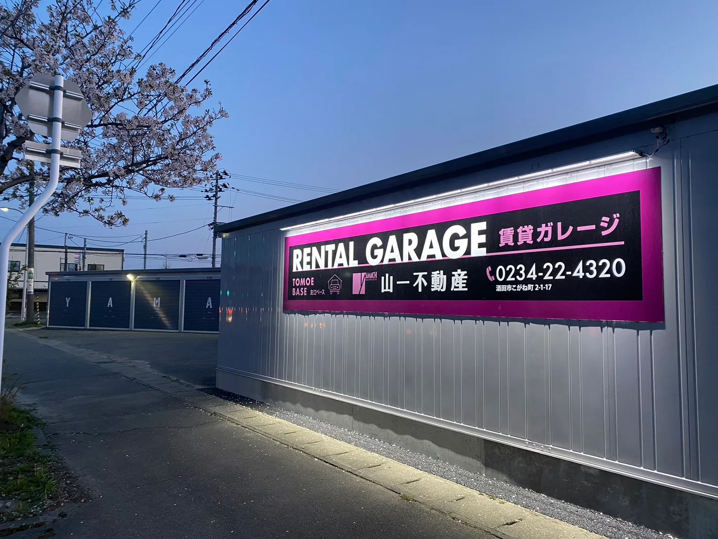 日が暮れた通りに面するガレージと、明かりのついたRENTAL GARAGEの看板